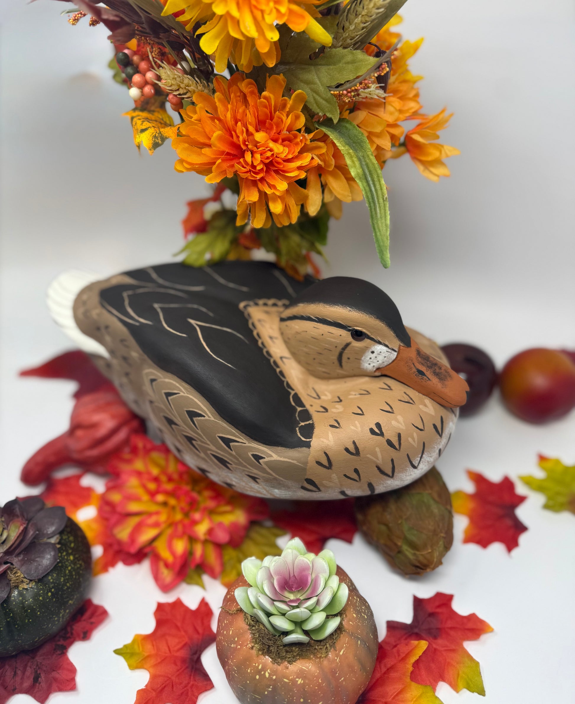 Decorative stone duck with autumn leaves, flowers, and fruits on a white background