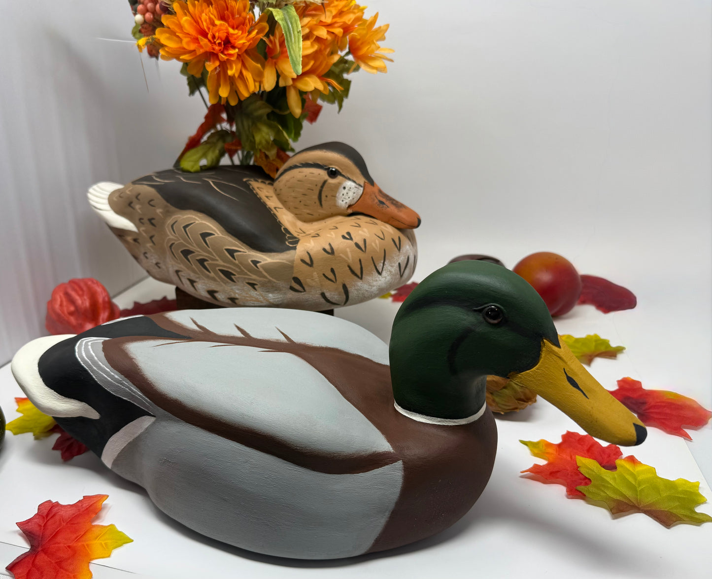 Two mallard duck figures with autumn leaves and flowers in the background